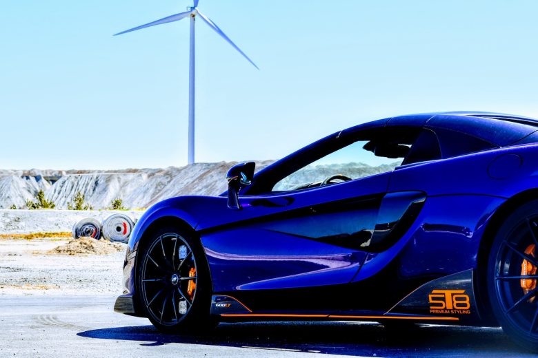 a blue sports car parked in front of a wind turbine